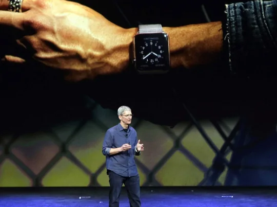 Tim Cook no palco da Apple, com a imagem gigante de um relógio inteligente num pulso atrás dele.