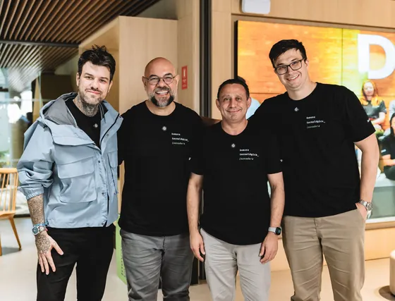 Gui Zanoni sorrindo ao lado de três homens de camiseta preta do time da Sicredi Dexis.