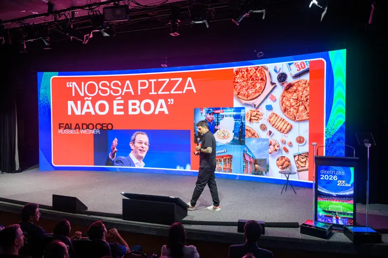 Gui Zanoni no palco de um congresso, com o telão Nossa pizza não é boa
