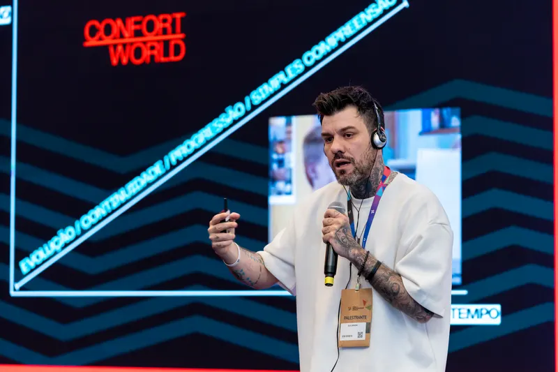 Gui Zanoni ao microfone num palco com telão vermelho e preto