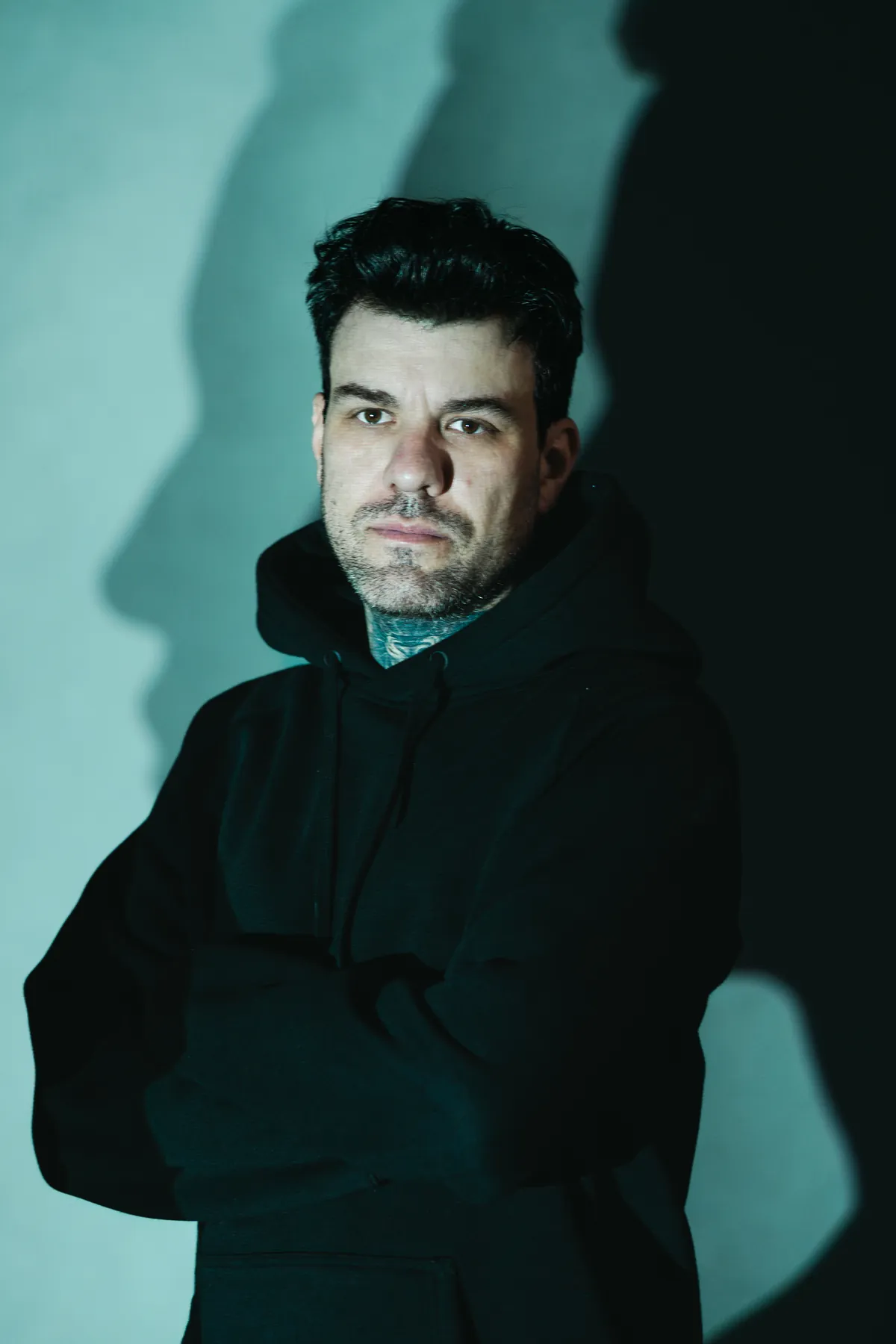 Gui Zanoni, de braços cruzados, em fundo escuro.